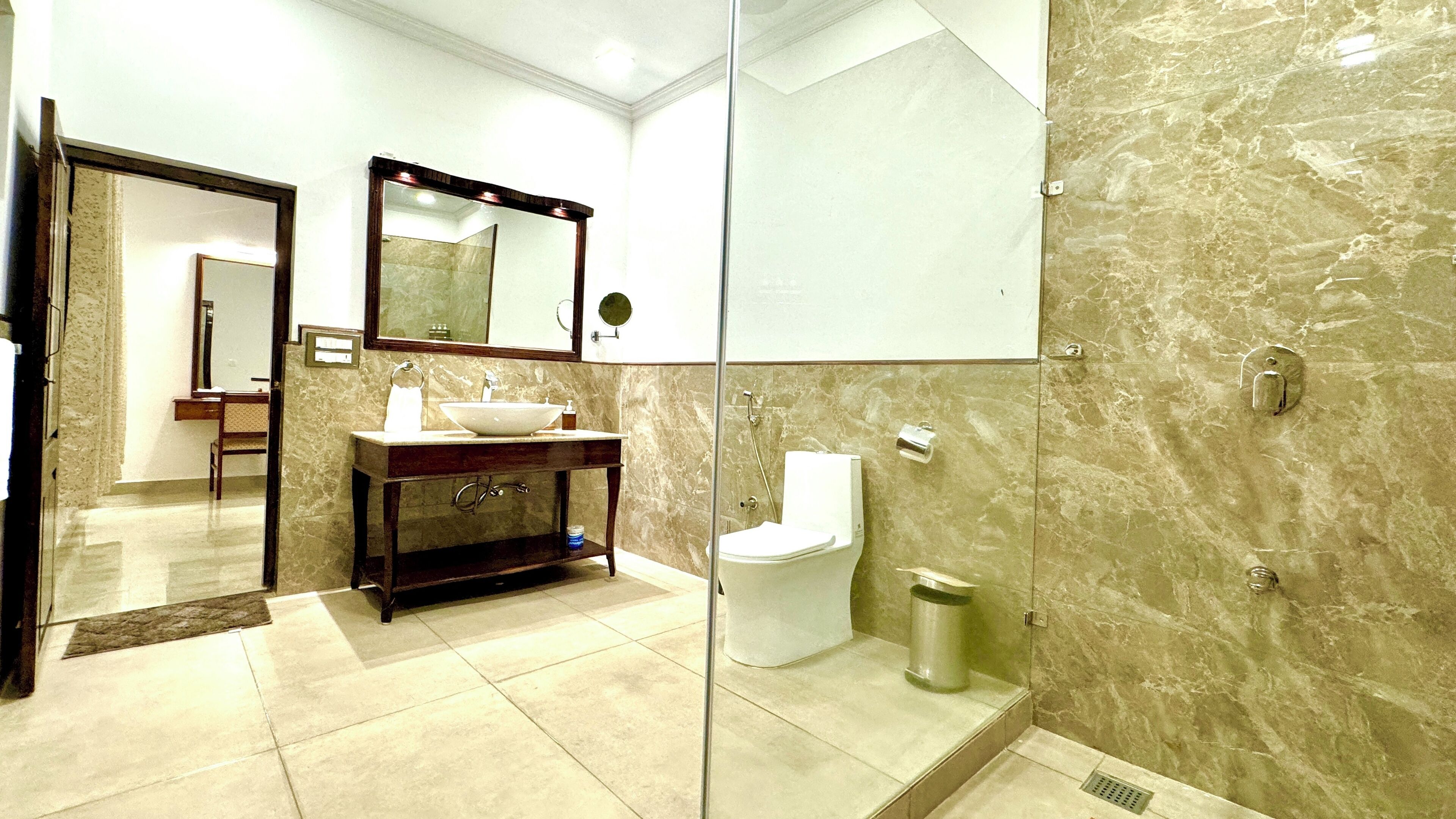 A modern bathroom with a marble sink, a large mirror, a toilet, and a shower area.