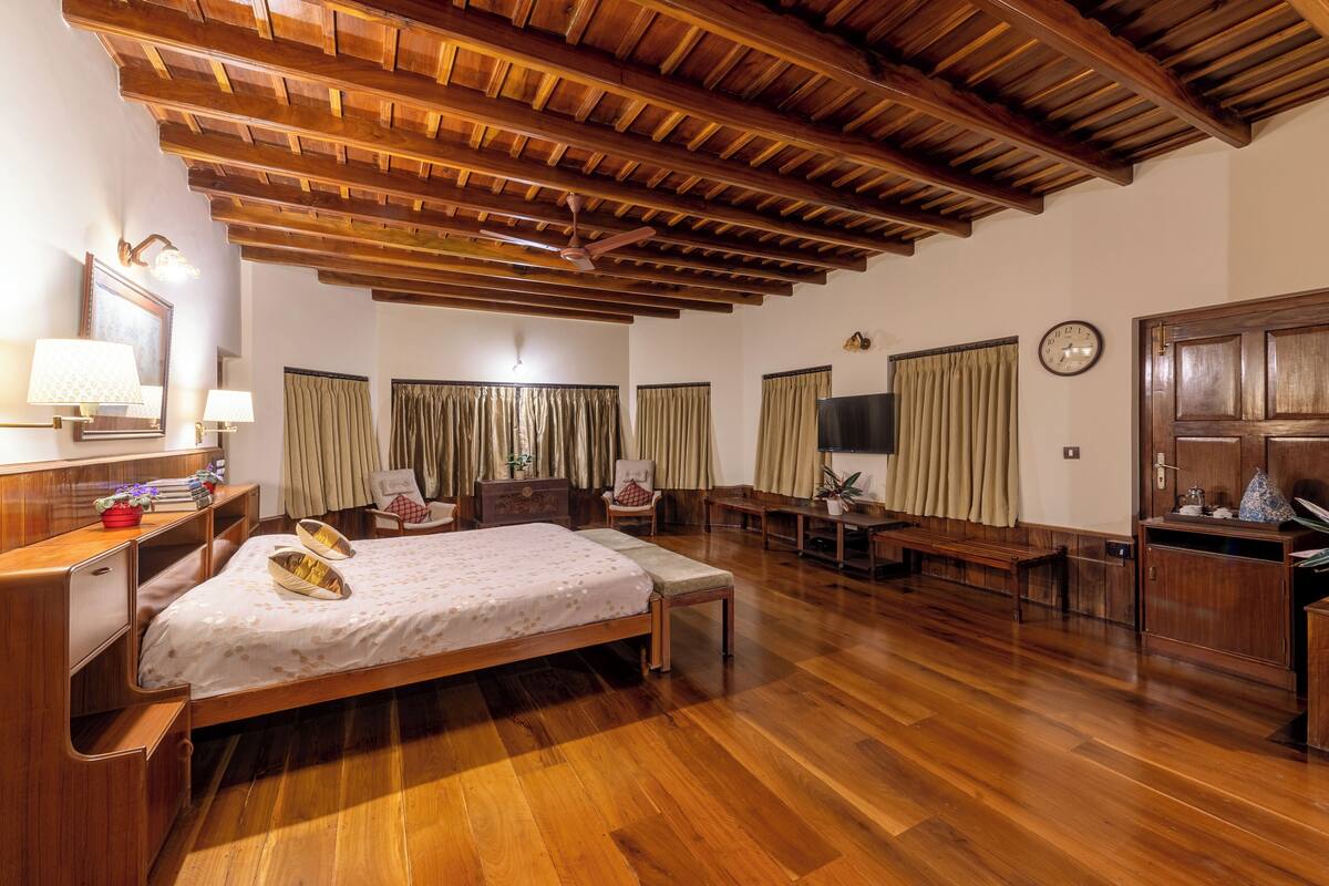 Una habitación amplia con techo de madera, una cama con dosel, un escritorio con silla y un televisor en la pared.