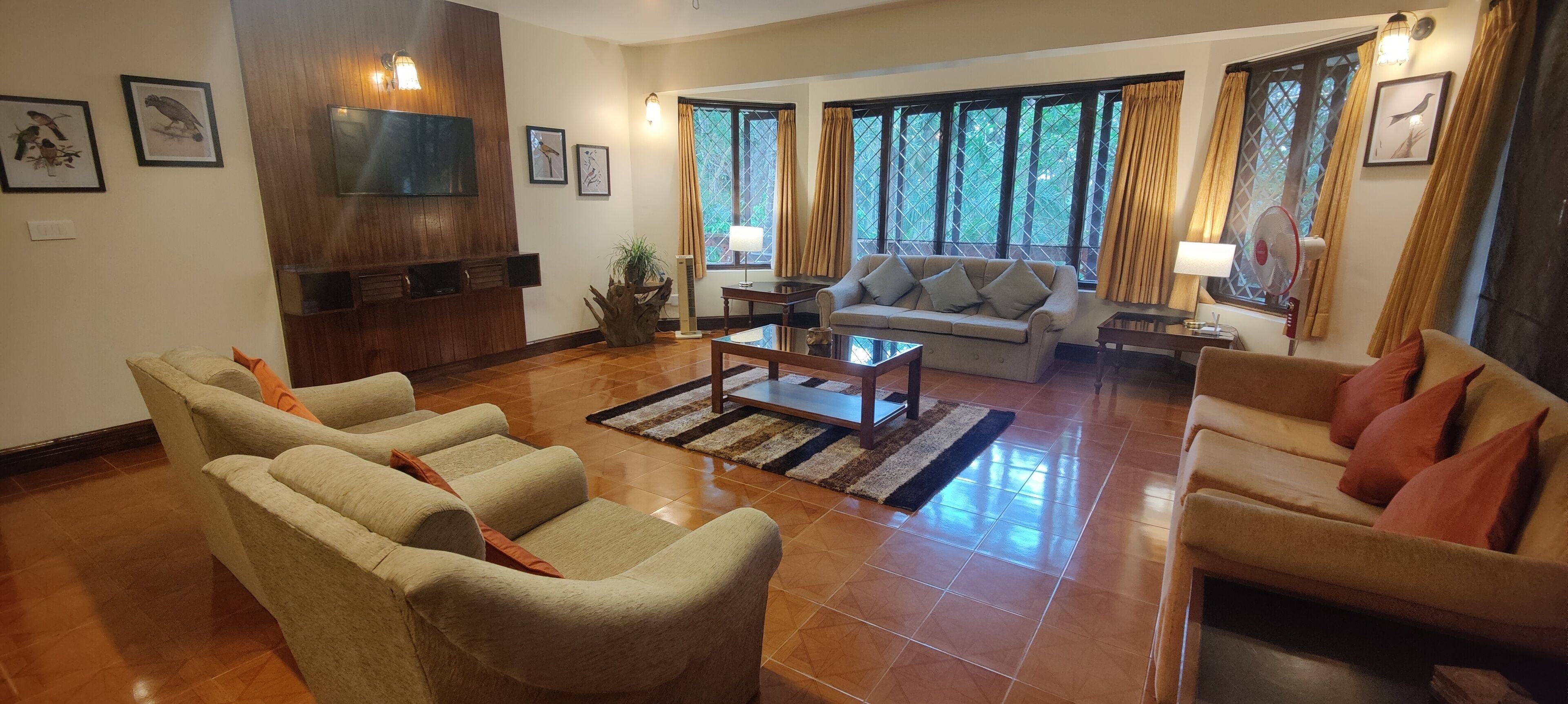 A spacious living room with a sofa, armchairs, a coffee table, and a TV mounted on the wall.