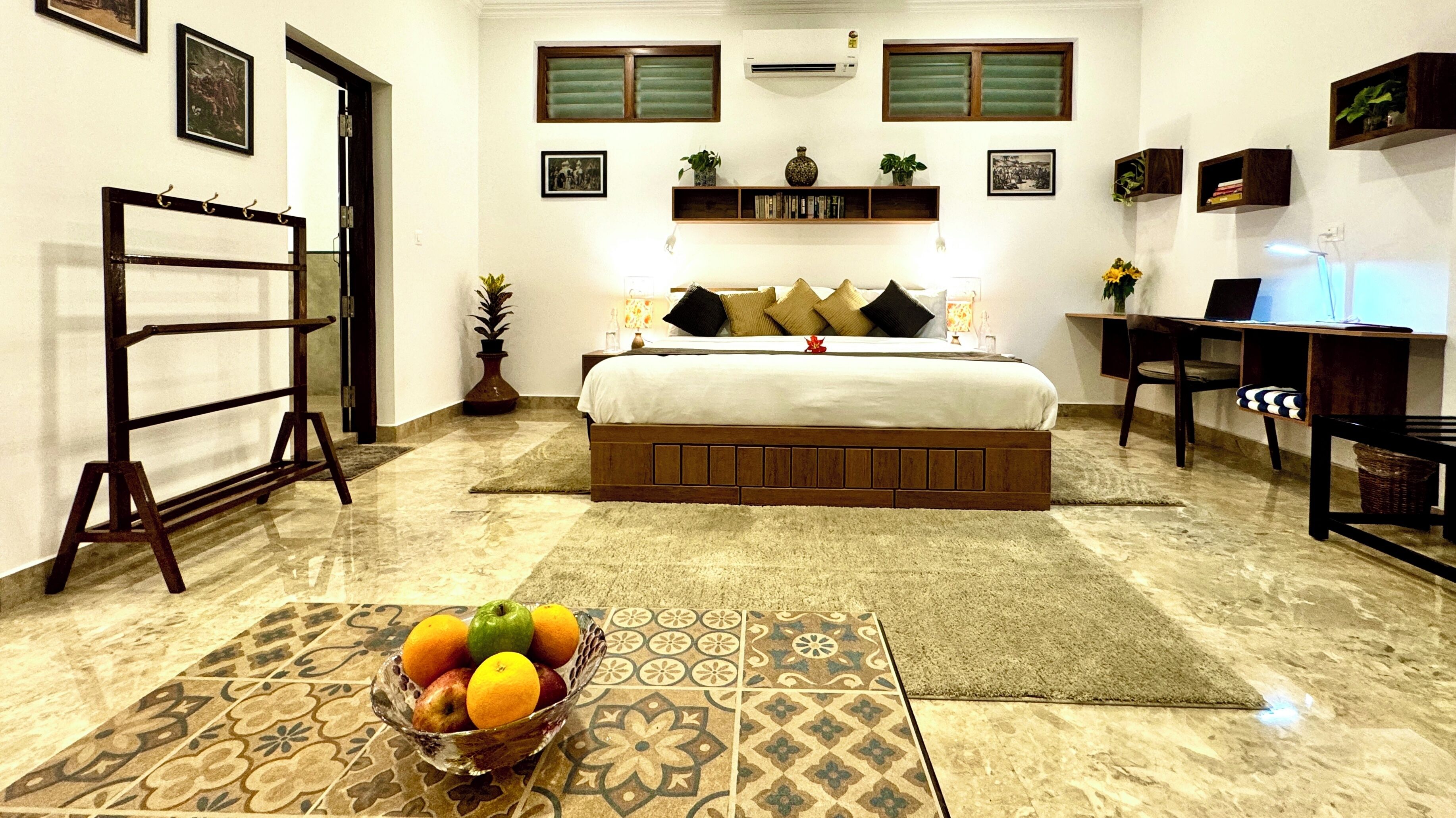 A hotel room with a bed, a desk, a chair, a fruit bowl, and a window.