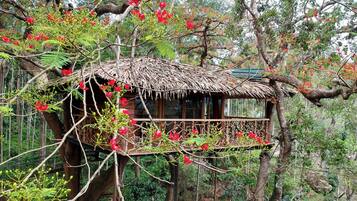 A treehouse with a thatched roof, surrounded by lush greenery and red flowers.