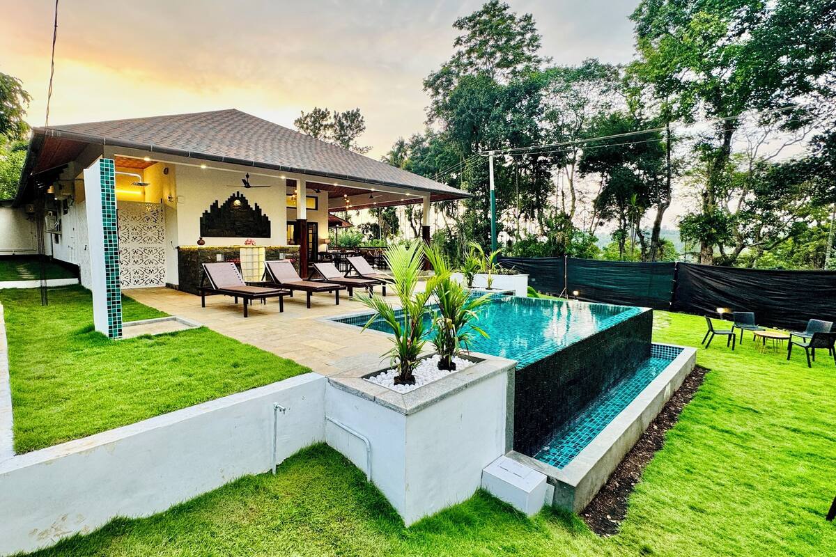 Un área de piscina moderna al aire libre con sillones de descanso, una zona de estar cubierta y un césped bien cuidado.