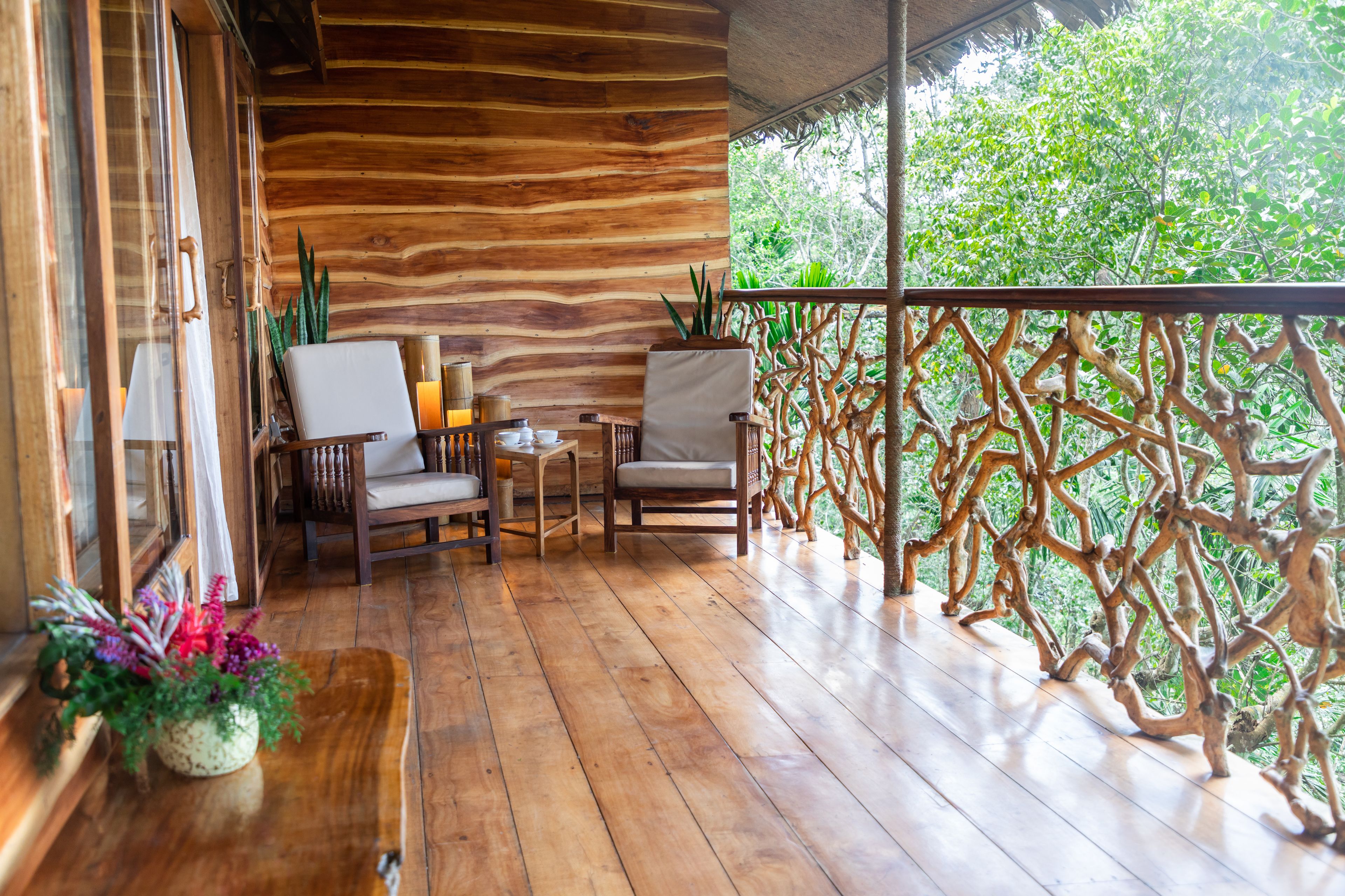 A wooden deck with two chairs and a table, surrounded by a wooden railing with a natural design.