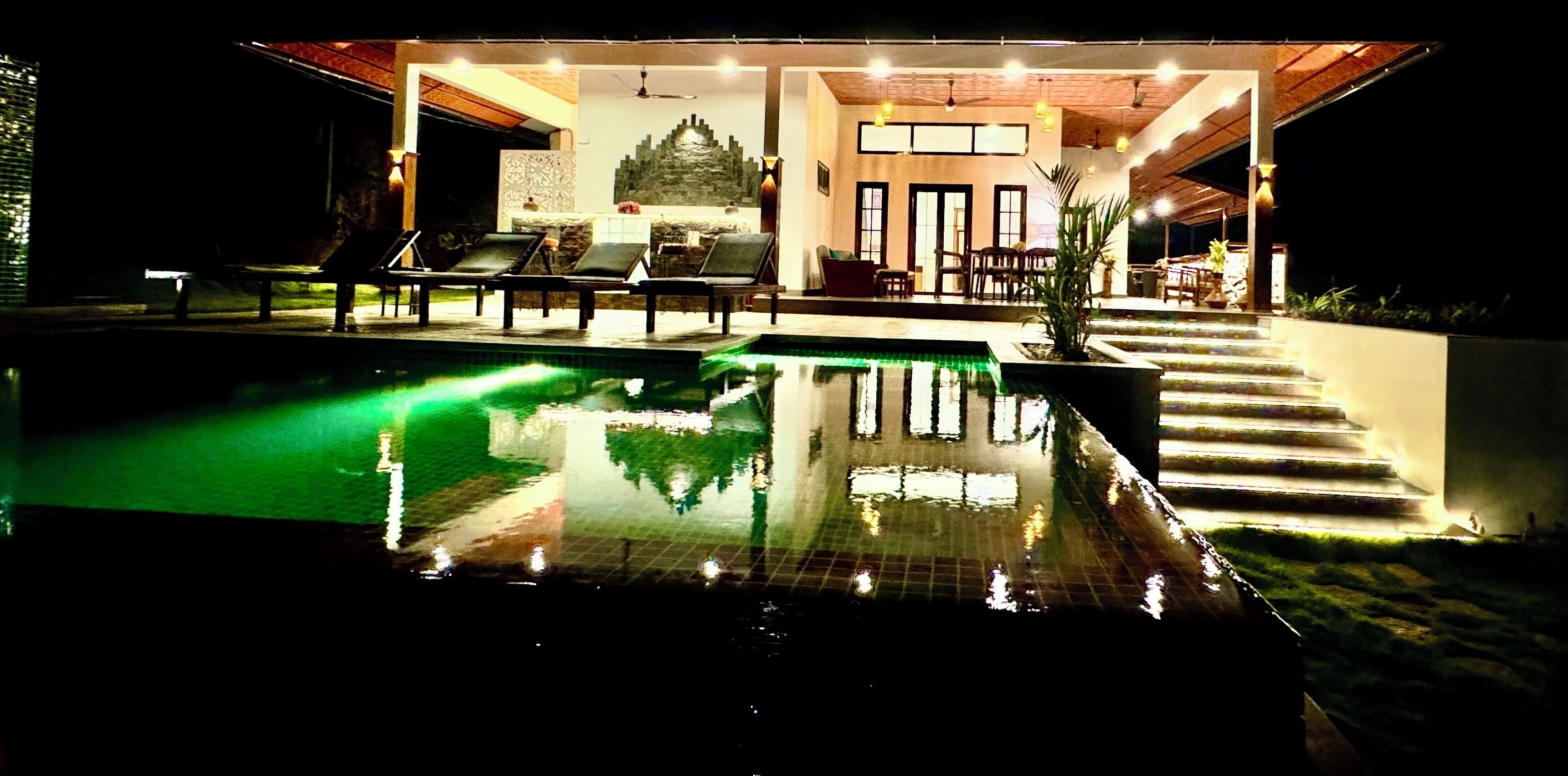 A pool area with lounge chairs and a staircase leading to a covered seating area.