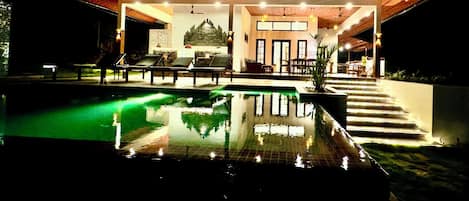 A pool area with lounge chairs and a staircase leading to a covered seating area.