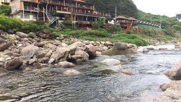 A river with rocks and a building with multiple levels and a red roof.