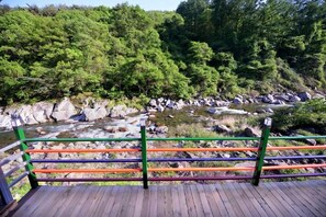 A wooden deck with a colorful railing overlooking a rocky riverbank and dense forest. - Jirisan Valley Pension (Namwon)