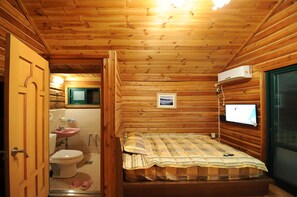 A wooden cabin room with a bed, a bathroom with a sink and toilet, and a television mounted on the wall. - Jirisan Valley Pension (Namwon)