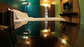 Een slaapkamer met een bed, een aan de muur bevestigde televisie en een spiegel die de kamer weerspiegelt.