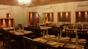 Een restaurant met houten tafels en stoelen, een kroonluchter en houten paneelwanden.