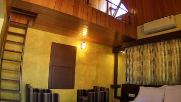 A hotel room with a wooden ceiling, a bed, a desk, a chair, a ladder, and a window.