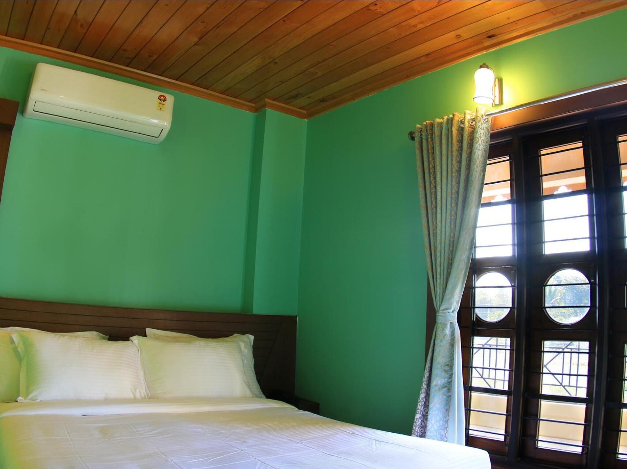 A room with a bed, an air conditioning unit, a window with curtains, and a wall with a green color.