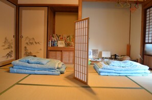 A traditional Japanese room with tatami flooring, a shoji screen, and a bookshelf with books and decorative items. - Satoyama Guest house COUTURE - Hostel (Ayabe)