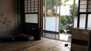 A room with wooden flooring, a futon bed, a heater, and a sliding glass door leading to a garden. - Satoyama Guest house COUTURE - Hostel (Ayabe)