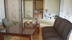 A traditional Japanese room with tatami flooring, a low wooden table, a brown sofa, and a shoji screen with artwork. - Satoyama Guest house COUTURE - Hostel (Ayabe)