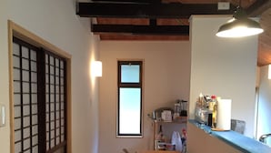 A narrow hallway with a wooden floor, a sliding door with a grid pattern, and a kitchen area with a counter and various items. - Satoyama Guest house COUTURE - Hostel (Ayabe)