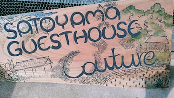 A wooden sign with the text "Sato-yama Guesthouse Culture" and illustrations of a house, trees, and a landscape.