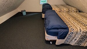 A small, enclosed attic room with a sloped ceiling, a single bed with patterned bedding, a small window, and a carpeted floor.