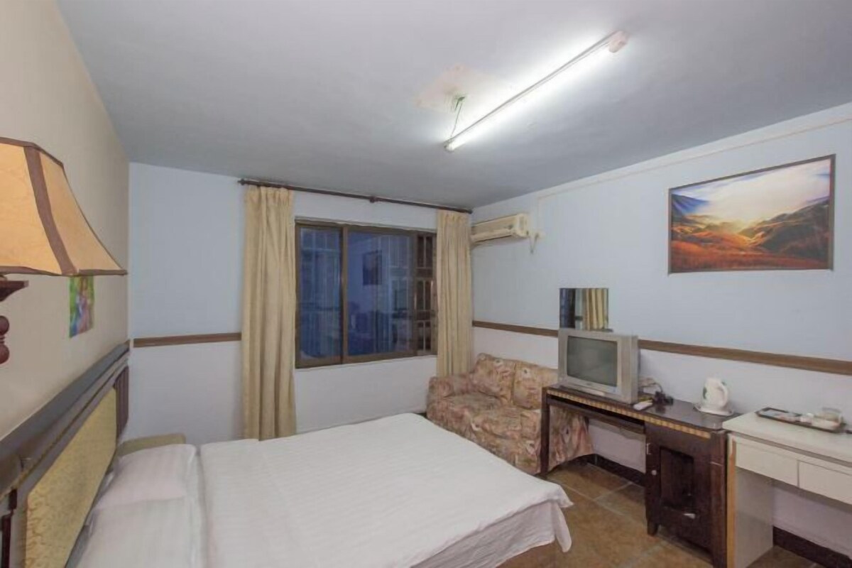 A hotel room with a bed, a desk with a television, a chair, and a window with curtains.