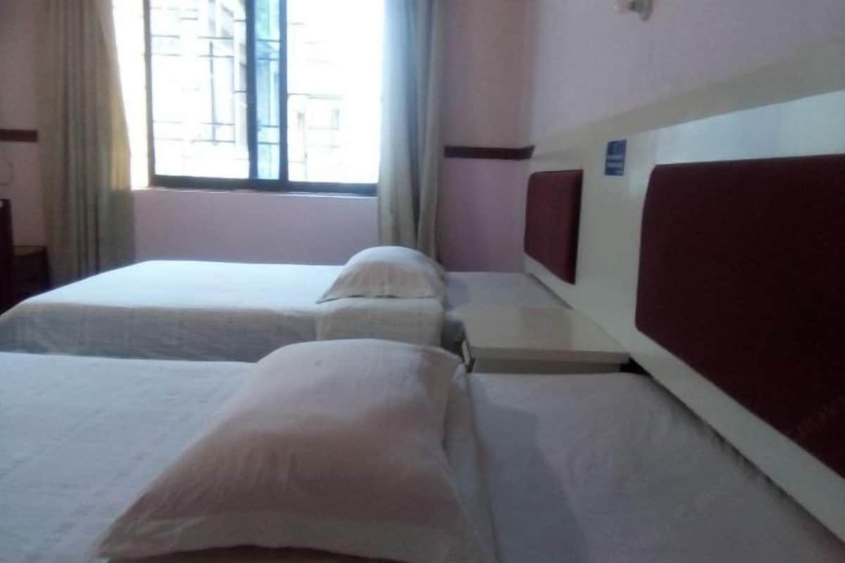 A hotel room with two single beds, a window with curtains, and a view of buildings outside.