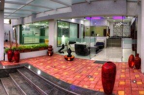 Un área de recepción con un separador de vidrio, asientos y jarrones decorativos.