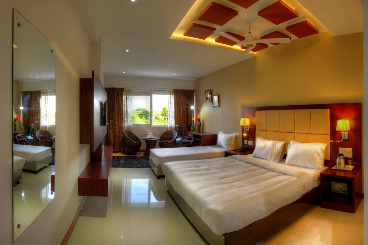 A hotel room with a large bed, a smaller bed, a desk with a chair, a sofa, a mirror, and a view of greenery outside.