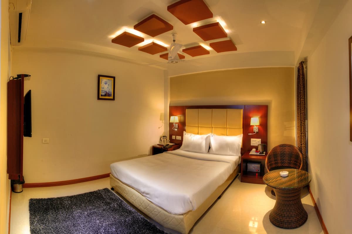 A hotel room with a large bed, bedside lamps, a ceiling fan, a small table with a lamp, and a mirror on the wall.
