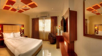 A hotel room with a large bed, a wooden dresser, a mirror, a television, and patterned curtains.