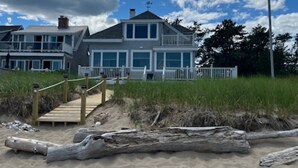 A beachfront property with a wooden staircase leading to a house with multiple windows and a balcony.