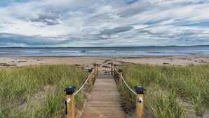 A wooden boardwalk leading to a beach with sand dunes and a cloudy sky.