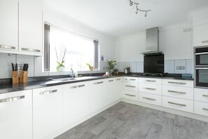 A modern kitchen with white cabinets, a black countertop, and a window with plants.