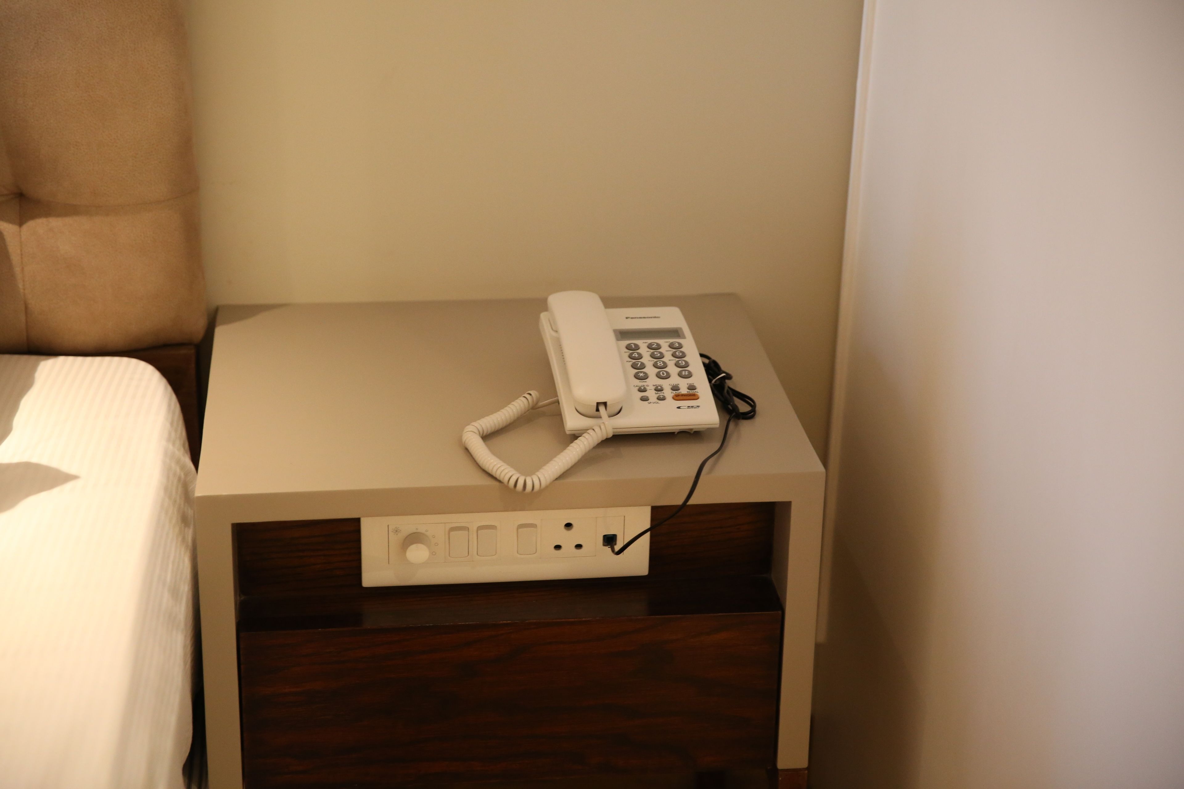 A hotel room with a bed, a bedside table with a telephone, and a power outlet.