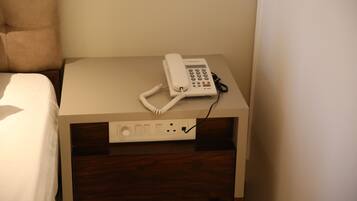 Quarto de hotel com uma cama, mesa de cabeceira com telefone e tomada.