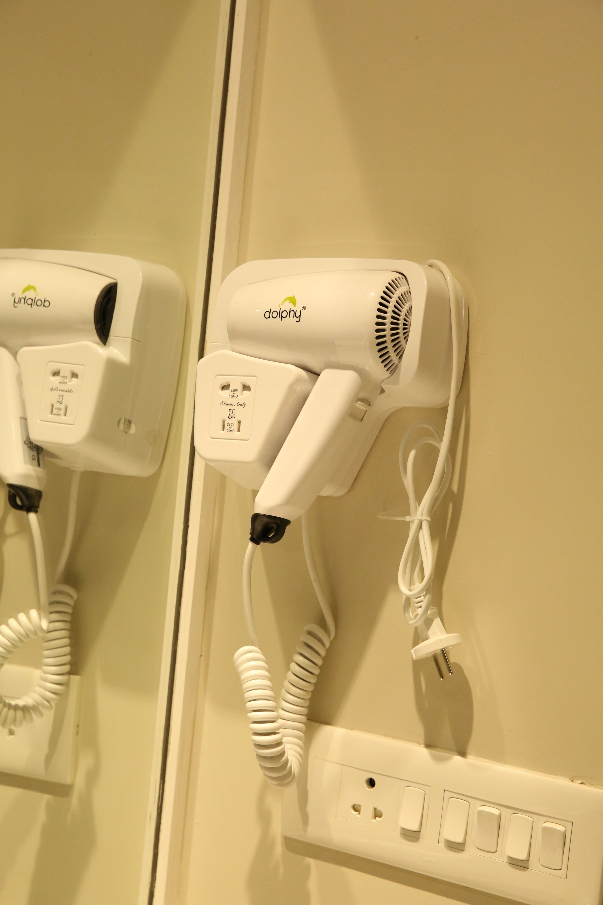 Two hair dryers mounted on a wall with a power outlet below them.