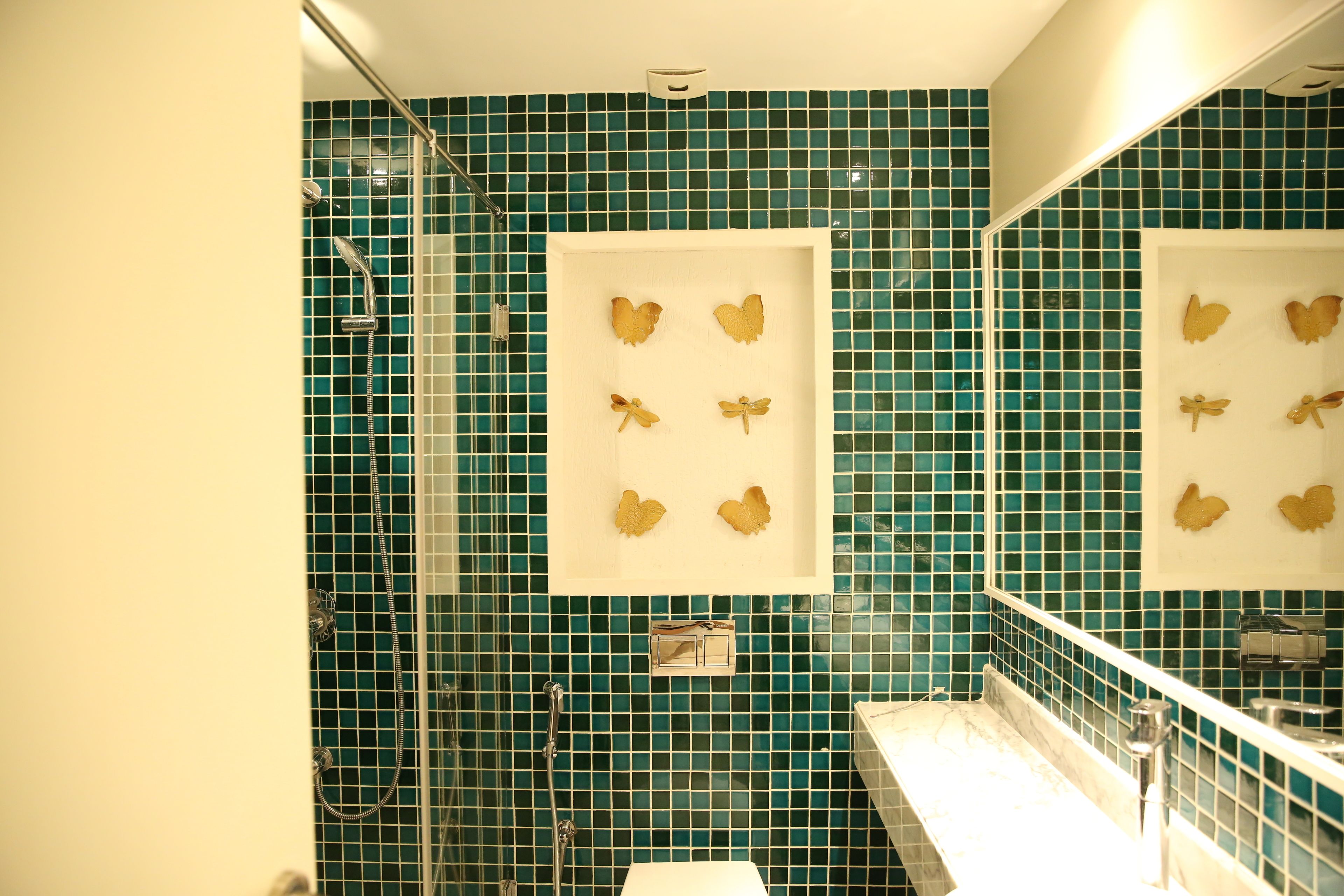 Une salle de bain avec des carreaux de mosaïque verts, une douche et un lavabo avec un miroir au-dessus.