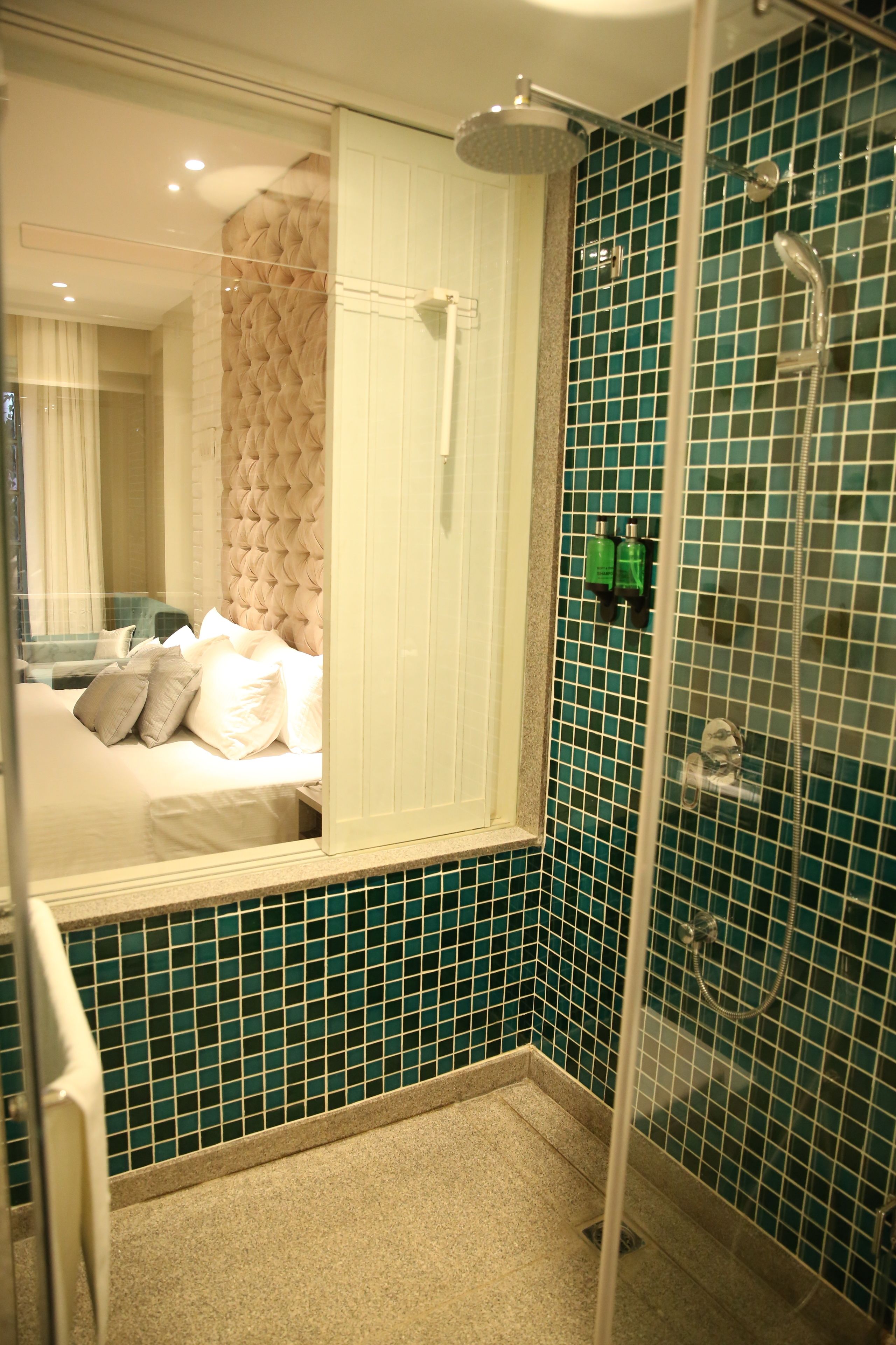 A bathroom with a shower, a bed with pillows, and a mirror.