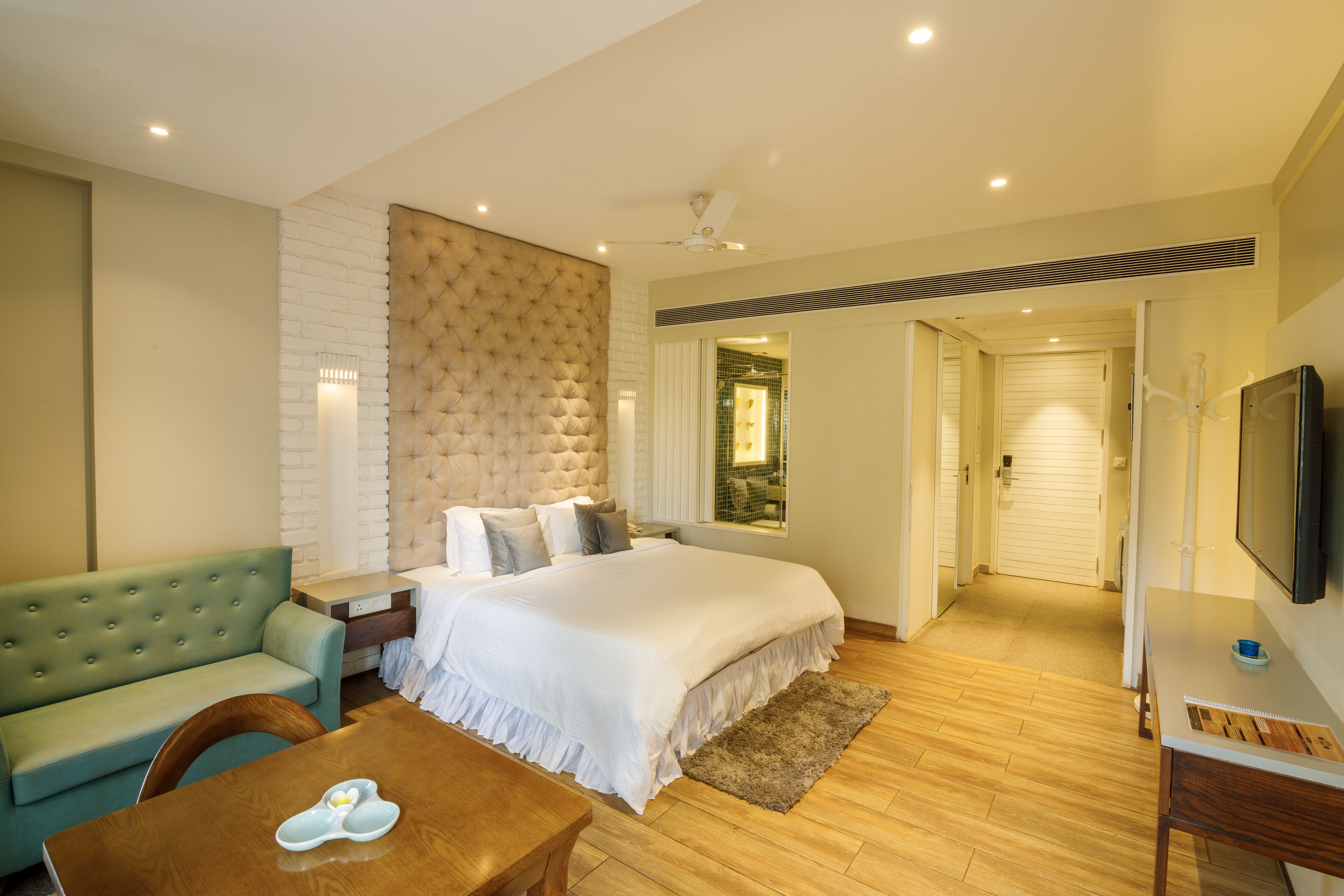 A bedroom with a large bed, a green sofa, a wooden table, and a TV on the wall.