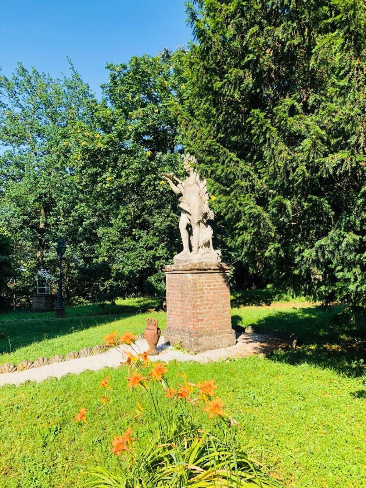 Eine Statue auf einem Sockel in einem Park mit grünem Rasen und Bäumen.