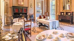 Une salle à manger élégante, avec plusieurs tables dressées pour le service, une cheminée et un décor classique.
