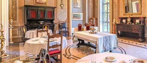 A formal dining room with multiple tables set for service, a fireplace, and classical decor.