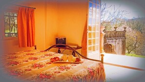 A bedroom with a bed, a tray with cups and a book, a window with curtains, and a view of a stone structure outside. - Charme of Villa Capannina (Novi Ligure)