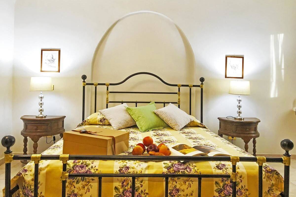 Ein Bett mit floralem Überwurf, zwei Kissen, ein Nachttisch mit Lampe und eine Schachtel auf dem Bett.