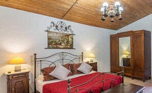 Una camera da letto con soffitto in legno, un letto con copripiumino rosso, due abat-jour, un armadio in legno e un quadro appeso al muro.
