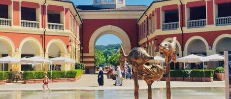 A courtyard with a fountain, red and white buildings, and a bell tower.