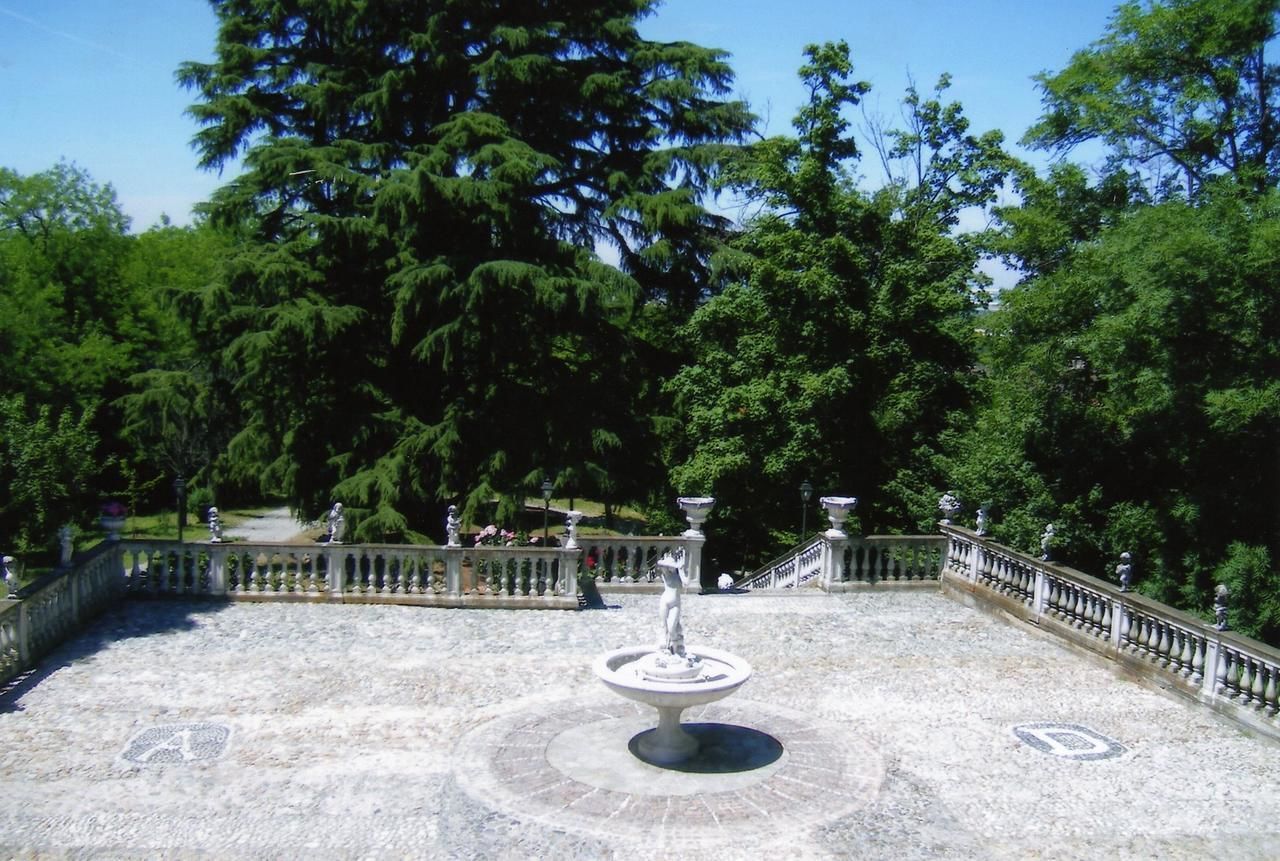 A fountain in a circular plaza surrounded by a stone balustrade, with trees in the background.