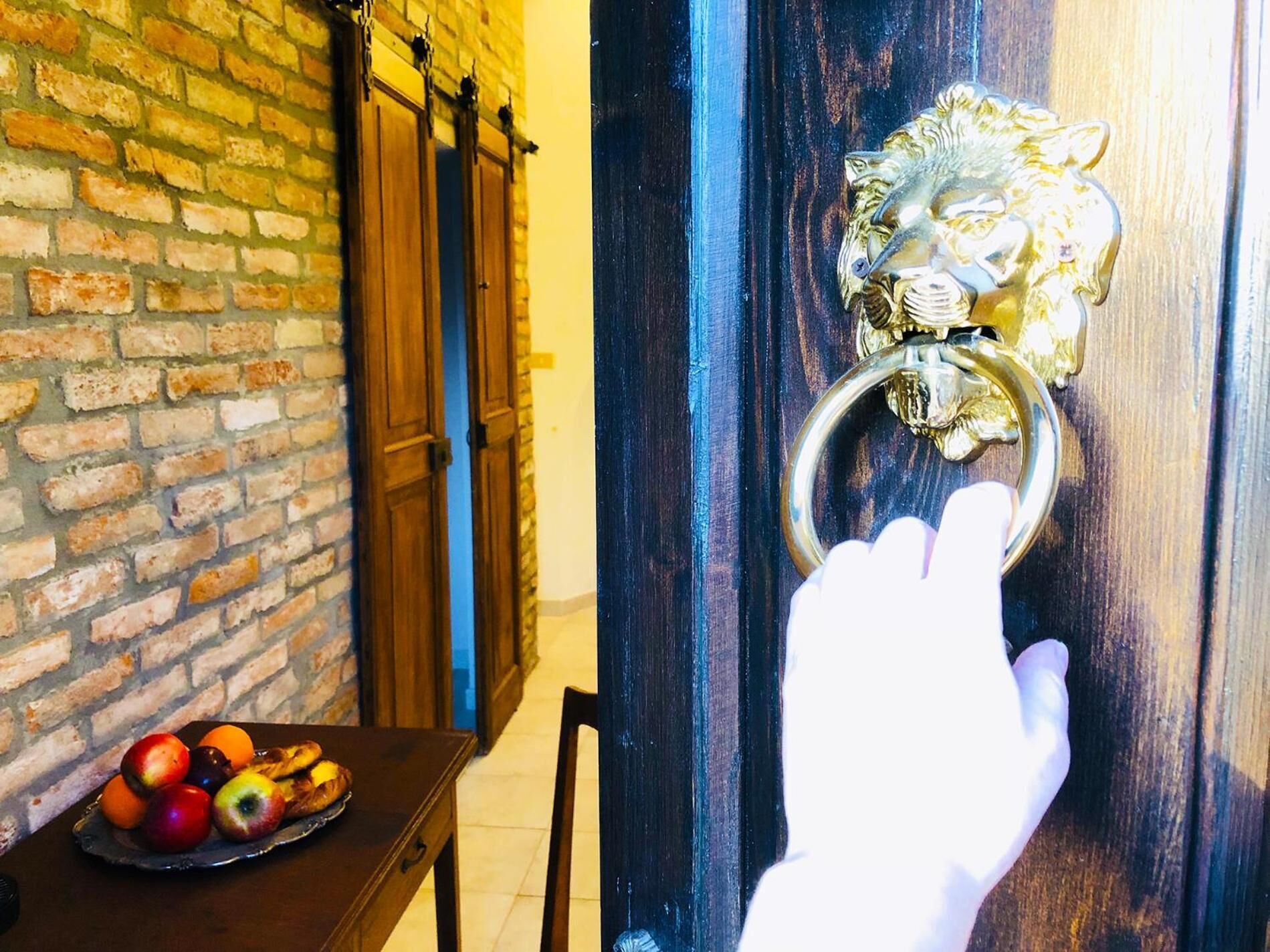 A hand reaching for a golden lion door knocker on a wooden door.