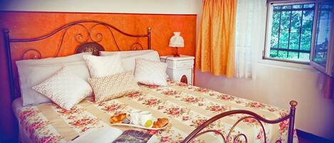 Una cama bien hecha con una colcha floral, una mesita de noche con lámpara y una ventana con cortinas.