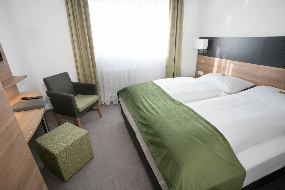 A hotel room with a bed, a desk, a chair, and a small ottoman.