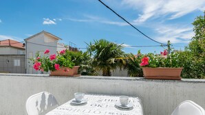 Een terras met een tafel gedekt voor twee personen, omringd door plantenpotten en een helderblauwe lucht.