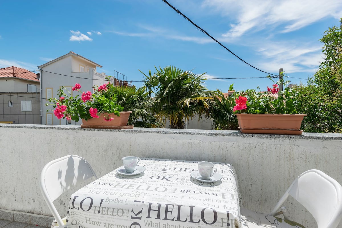 A terrace with a table set for two, surrounded by potted plants and a clear blue sky.
